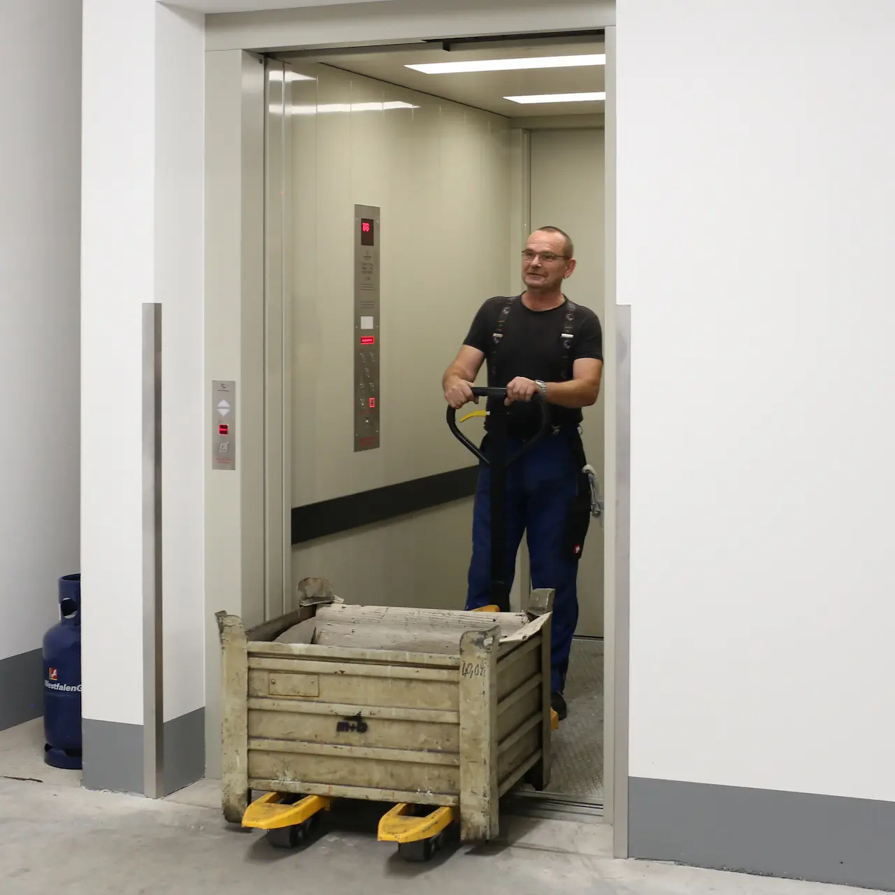 Mitarbeiter transportiert Material mit Hubwagen aus Lastenaufzug für innerbetrieblichen Warenfluss.