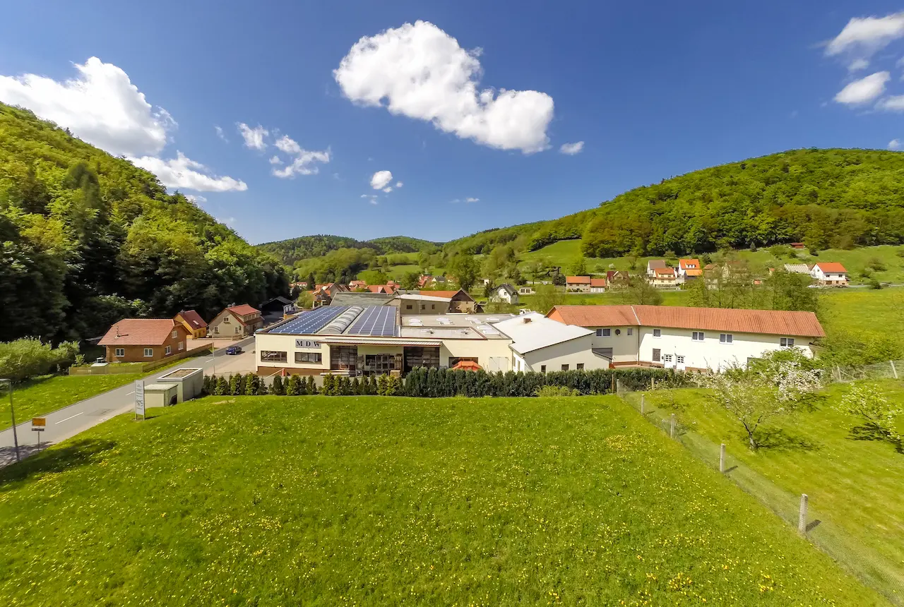Luftaufnahme des MDW Firmengebäudes mit Solaranlage und grüner Umgebung.