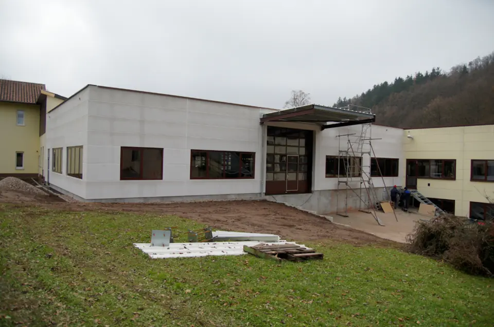 Außenansicht des Neubaus mit Gerüst und unbefestigtem Gelände.